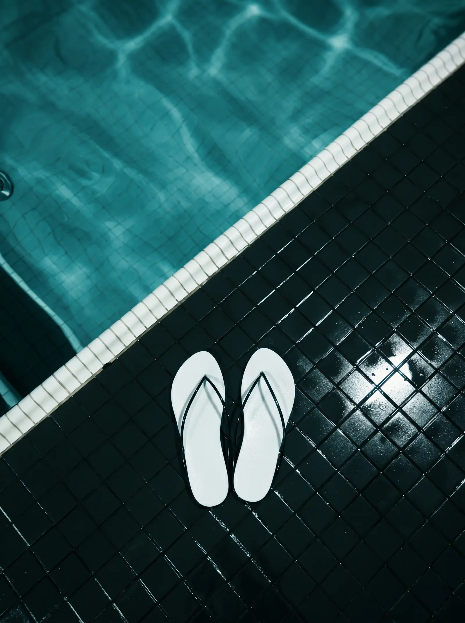 Weiße Slipper am Pool auf dunklen Fliesen
